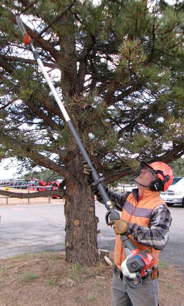 Man operating Husqvarna Pole Saw in protective eye gear and vest at Hitchin Post Rentals