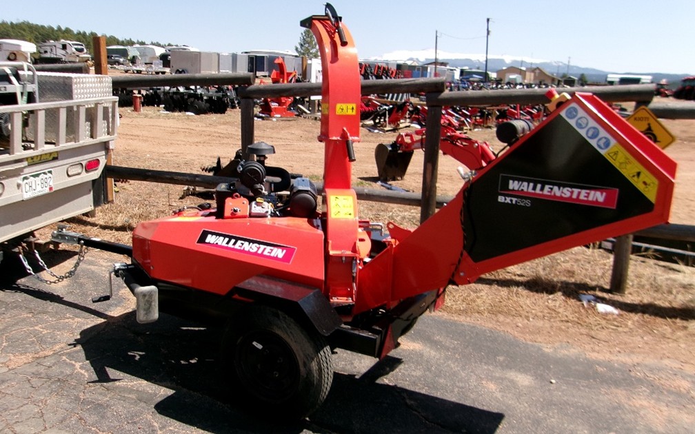 Wallenstein Wood Chipper sitting on cement next to fence and trailers.