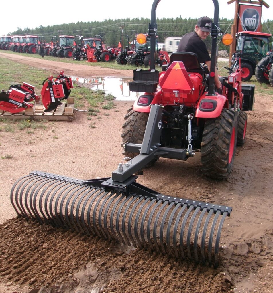 man sitting on 24HP KIOTI Compact Tractor and Landscape Rake working in dirt lot